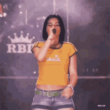 a woman is singing into a microphone wearing a yellow shirt that says brasil