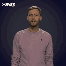 a man in a pink sweater is making a funny face in front of a blue background with swr3 written on it