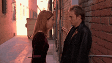 a man and a woman lean against a brick wall in an alleyway