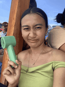 a woman in a green off the shoulder top is holding a small green fan