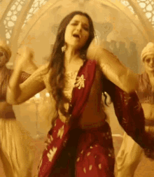 a woman in a red saree is dancing in a room with other people .
