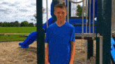 a boy in a blue shirt stands in front of a playground set