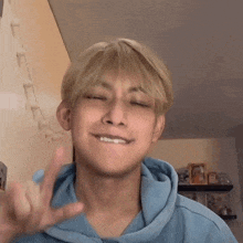 a young man wearing a blue hoodie is making a peace sign with his fingers