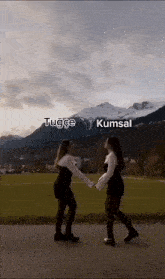 two girls are holding hands in front of a mountain with the words tugce kumsal written on the bottom