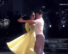 a woman in a yellow dress is hugging a man