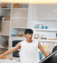 a man in a white tank top standing in a kitchen