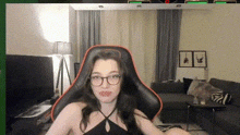 a woman wearing glasses and a black top is sitting in a gaming chair .