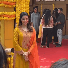 a woman in a yellow and orange dress is standing on a red carpet in front of a group of people .