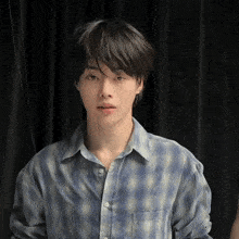 a young man wearing a blue plaid shirt is looking at the camera