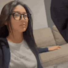 a woman wearing glasses is sitting on a couch looking at the camera .