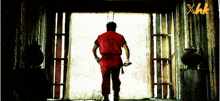 a man in a red shirt is standing in a doorway with a xhk logo in the corner