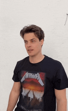 a man wearing a black metallica t-shirt is standing in front of a white wall
