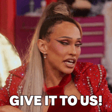 a woman in a red jacket and tie is saying give it to us