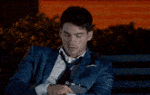 a man in a suit and tie is sitting on a bench with his eyes closed holding a flask .