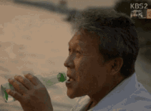 a man drinking from a green bottle with kbs2 on the bottom