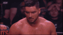 a shirtless wrestler is smiling in front of a crowd with aew written on the screen behind him .