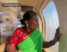 a woman in a green and red saree is sitting on an airplane .