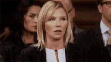 a woman in a suit and white polka dot shirt looks shocked