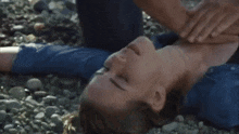 a woman is laying on the ground with her eyes closed and a man is giving her a heart massage .