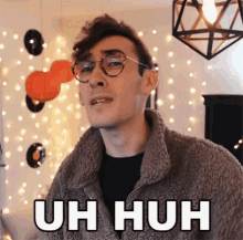 a young man wearing glasses and a sherpa jacket is making a funny face and says uh huh .
