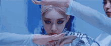 a woman with blonde hair and red lips is sitting in front of a blue wall with her hands on her chin .