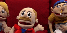three stuffed animals are sitting on a red couch and one has a pencil in his nose .