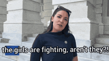 a woman is standing in front of a building with the words " the girls are fighting aren 't they "