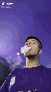 a man in a purple shirt is smoking an electronic cigarette against a purple sky .