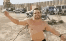 a shirtless man is standing in the sand with his arms outstretched in front of a fence .