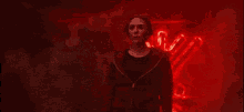 a woman in a red jacket is standing in front of a red wall with a symbol on it .