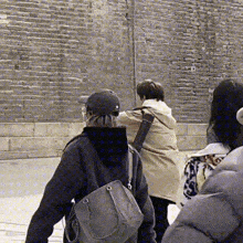 three people are walking in front of a brick wall .