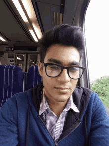 a man wearing glasses and a blue jacket sits in a train car