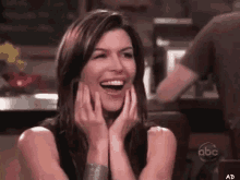 a woman is laughing with her hands on her face while sitting at a table in front of a sign that says abc