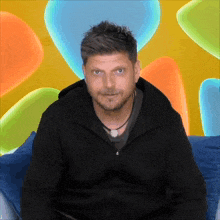 a man in a black jacket is sitting in front of a colorful background of balloons