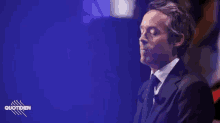 a man in a suit and tie is standing in front of a blue background with the word quotidien on it