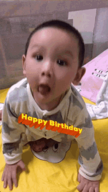 a baby is crawling on a bed with a happy birthday sticker on it