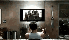 a man is sitting on a couch watching a movie on a flat screen television .