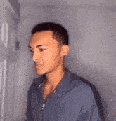 a man in a blue shirt is standing in front of a door and making a face .