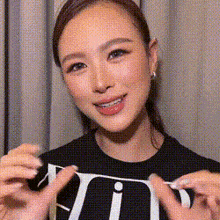 a woman wearing a black t-shirt with the letter v on it is smiling and holding a piece of paper .