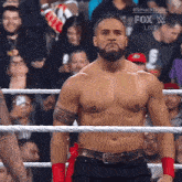 a shirtless wrestler is standing in a ring with a fox live advertisement behind him