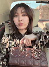 a woman is sitting in a car holding a brown purse and making a face