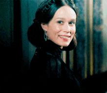 a woman wearing a black dress and earrings smiles at the camera
