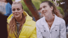 two girls are sitting next to each other and the letters m + are on the bottom right