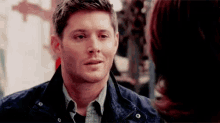 a man in a blue jacket is looking at a woman in a black shirt .