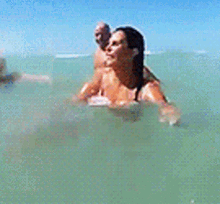 a woman in a bikini is swimming in the ocean while a man watches .