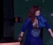 a woman in a blue dress is dancing on a stage with a microphone .