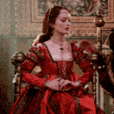 a woman in a red dress with a cross necklace is sitting on a chair