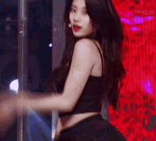 a woman in a black crop top is dancing in front of a red background ..