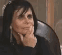 a woman is sitting in a chair with her hand on her chin and looking at the camera .