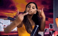 ariana grande is wearing a yellow tank top and holding a black object .